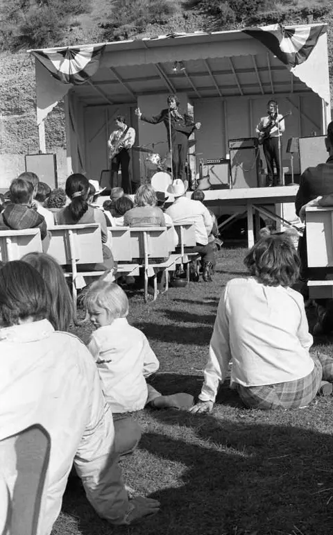 Black and white photo of a band playing on a stage for an outdoor audience.
