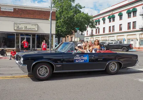 A convertible car carrying people in a parade down a street.