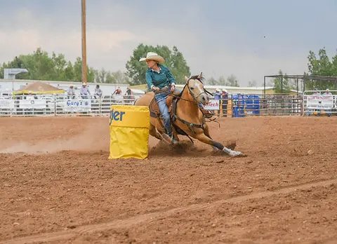 A cowgirl rounds a yellow barrel on a horse during a rodeo event.