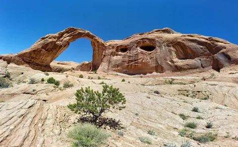 A large natural rock arch stands in a desert landscape.