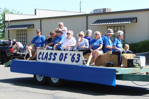A group of people ride on a parade float with a sign reading class of 63.