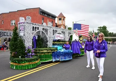 A parade float passes down a street with people walking alongside.
