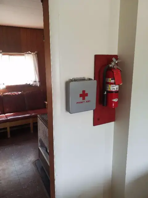 A first aid kit and a fire extinguisher mounted on a wall indoors.