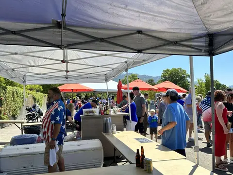 People gather under canopies at an outdoor event on a sunny day.