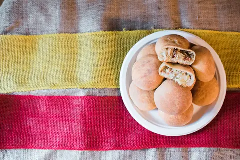 A plate of baked buns, with some cut open to show the filling, rests on a textured surface.