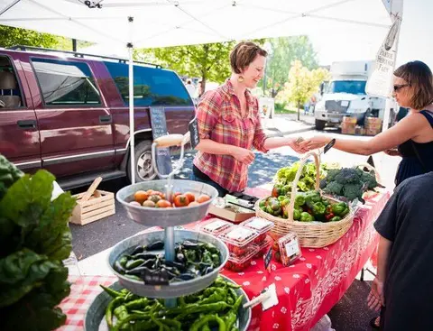 A woman sells vegetables at an outdoor market stall.