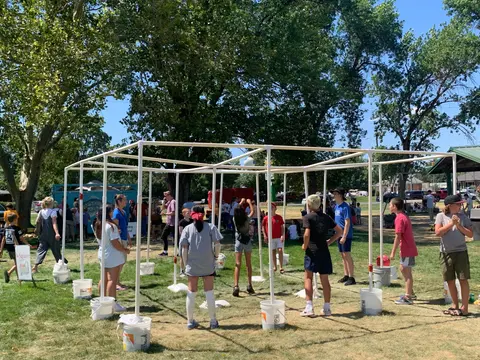 People playing 9-square in a park with a PVC pipe frame.