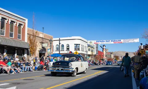 A vintage police car drives down a street lined with spectators during a parade under a clear blue sky.