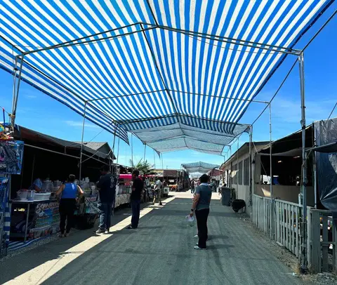 An outdoor marketplace with blue and white striped awnings over a pathway between vendor stalls.