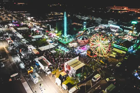 An aerial view of a brightly lit nighttime carnival with rides and crowds.