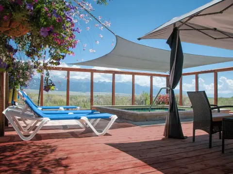 A wooden deck features lounge chairs, a hot tub, sun shades, and a scenic mountain view in the background.