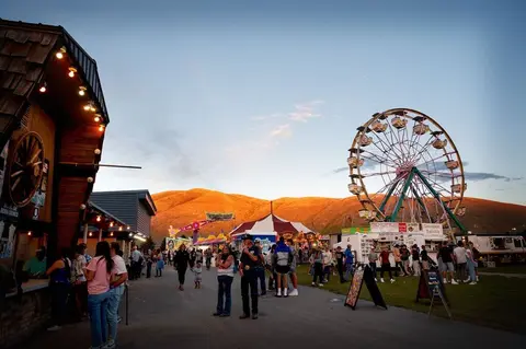 A carnival with a Ferris wheel and people walking around at dusk.