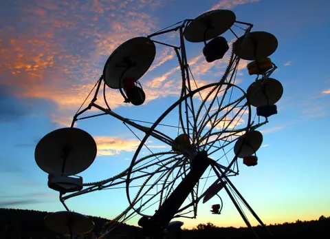 A silhouette of a carnival ride against a sunset sky.