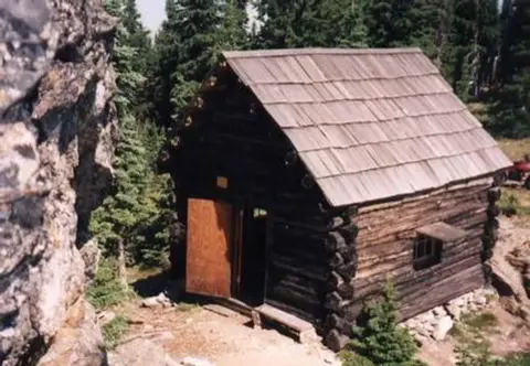 A small log cabin stands in a wooded area.