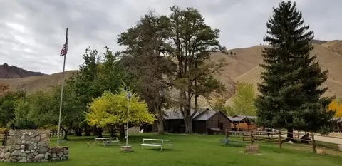 An outdoor area with a flag, picnic tables, trees, and hills in the background.