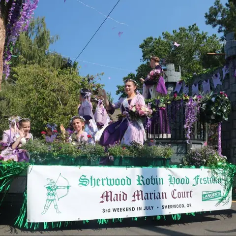 A parade float features people in medieval-style purple dresses.