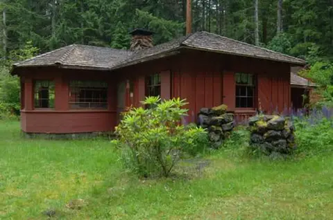 A red wooden cabin sits in a clearing surrounded by trees.