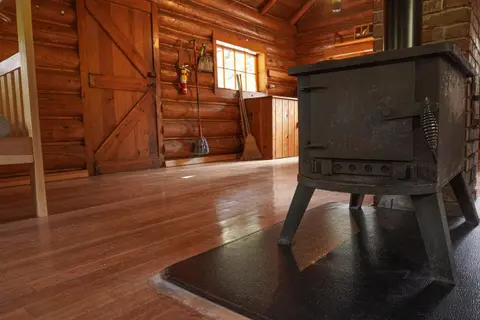 Interior of a rustic log cabin featuring a wood-burning stove on the floor.