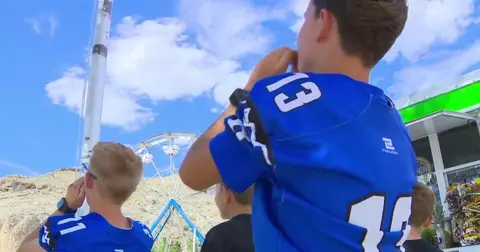 Boys wearing blue jerseys look up at an outdoor attraction.