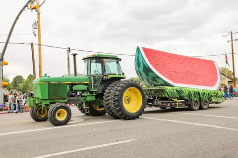 A tractor pulls a large float shaped like a watermelon slice on a street.