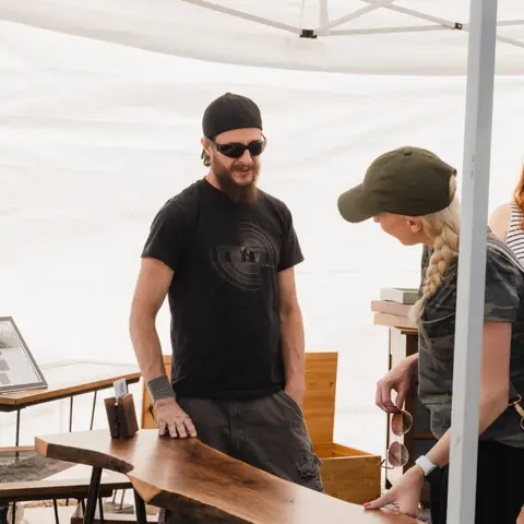 A man and woman talking at an outdoor craft booth.