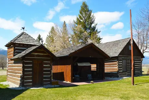 Exterior view of historic log cabins on a grassy lawn.