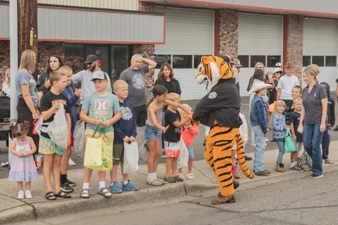 A costumed tiger mascot interacts with children outside a building.