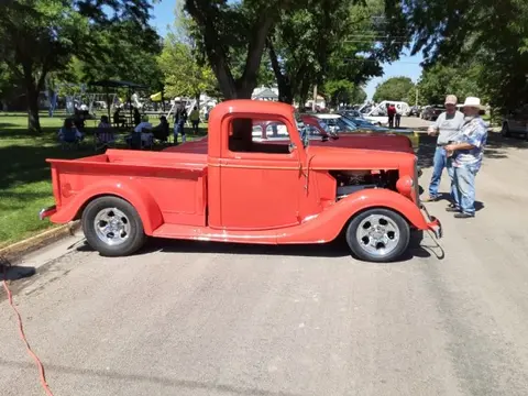 A vintage red pickup truck parked on a street near a park.