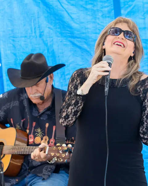 A woman sings into a microphone while a man plays an acoustic guitar.