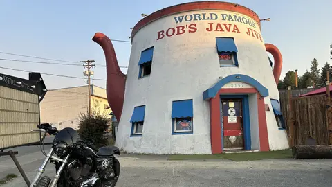 A photo of a building shaped like a giant teapot with a motorcycle parked in front.