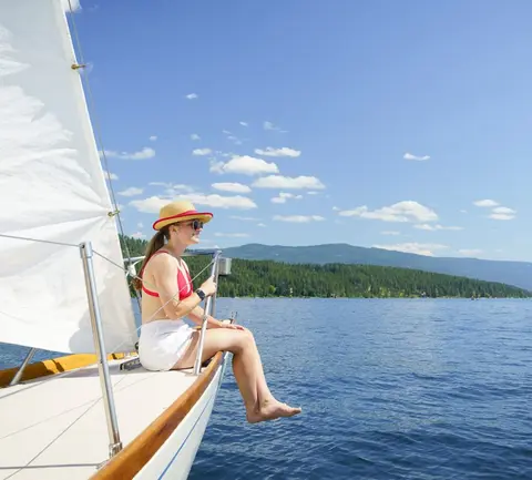 A woman sits on the bow of a sailboat on a lake.