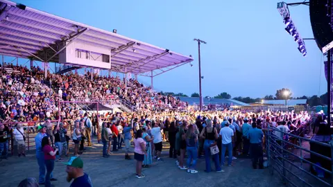 A large crowd of people gathered in front of grandstands at an outdoor venue during twilight.