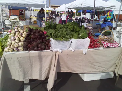 A table at an outdoor market displays various fresh vegetables.