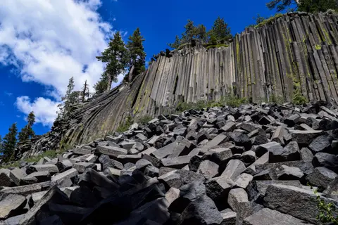 A tall cliff of columnar basalt rock formations with a pile of fallen polygonal blocks at the base.