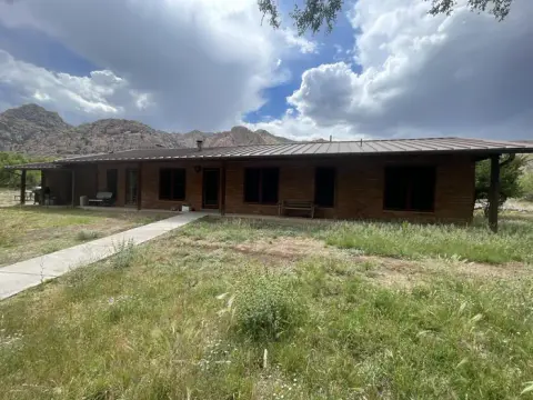 A single-story brick building stands before a mountain range under a cloudy sky.