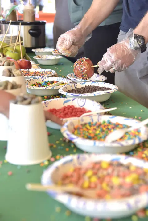 People preparing caramel apples with various toppings at a station.