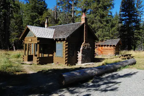 A historic log cabin and outbuilding surrounded by a forest.