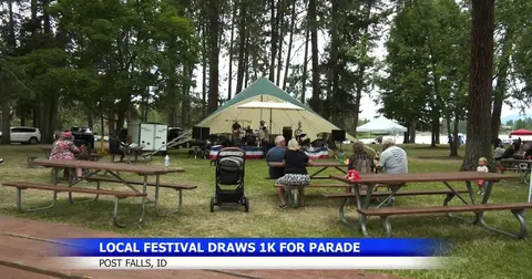 People sit at picnic tables in a park while a band performs under a canopy.