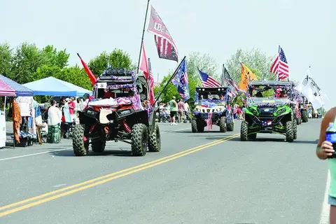 Decorated off-road vehicles drive down a street during a parade.
