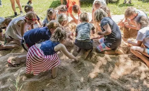 A group of children playing in a pile of sand or wood shavings outdoors.
