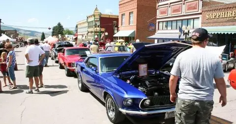 A street scene during a classic car show with people looking at vehicles.