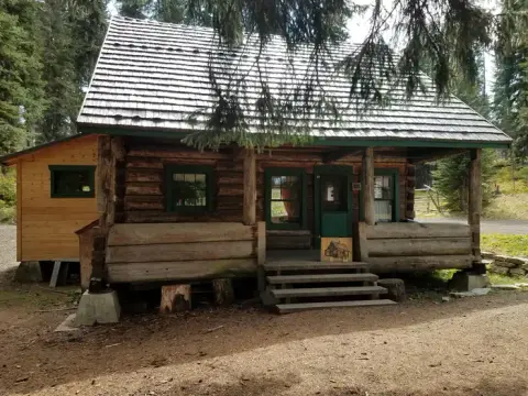 A rustic wooden cabin with a shingled roof stands among trees.