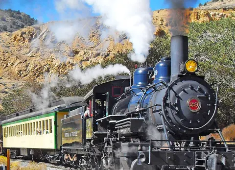 A steam train travels through a mountainous landscape.