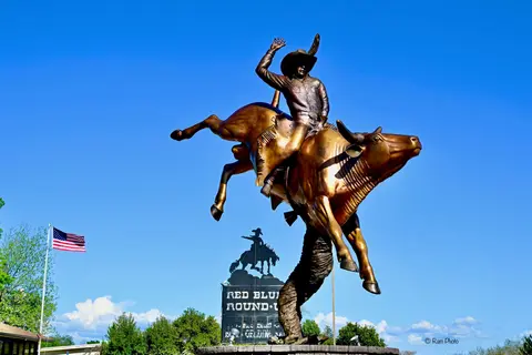 A large bronze statue of a cowboy riding a bucking bull outdoors.