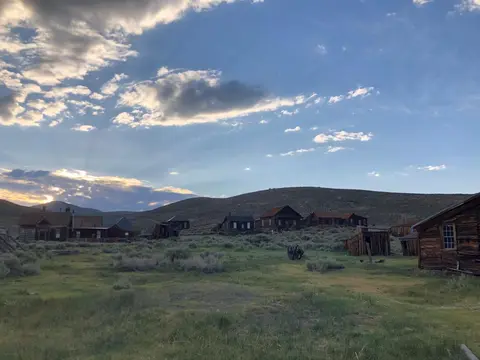 An old wooden ghost town set against rolling hills and a cloudy sky.