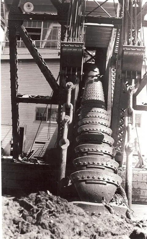 A historic black and white photograph showing the bucket line of a large industrial dredge.