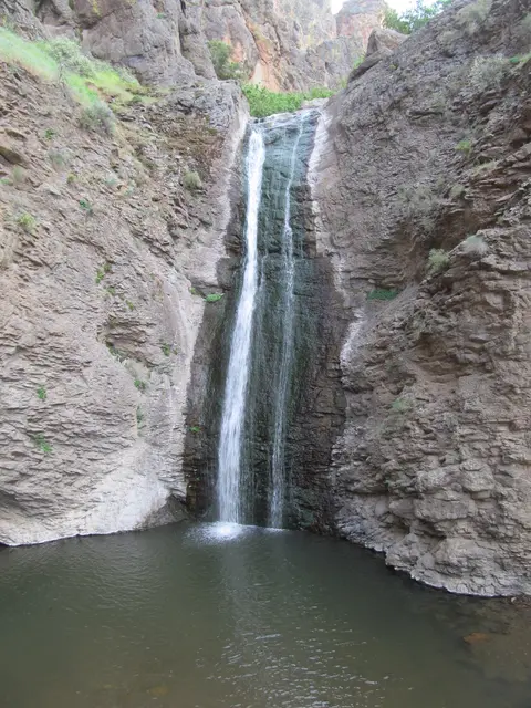 A waterfall flows into a pool surrounded by rocky cliffs.