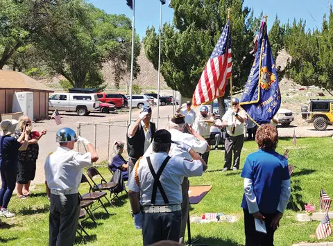 A group of people saluting during an outdoor ceremony with American flags.