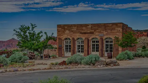 A stone building with arched doorways stands in an arid landscape under a blue sky.