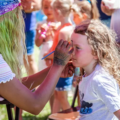 A face painter paints the face of a young girl.